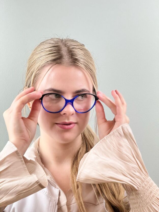 Młoda kobieta z jasnymi włosami próbuje nowych okularów o niebieskich oprawkach w salonie optycznym